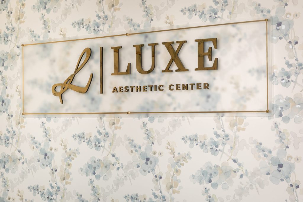 Luxe Aesthetic Center sign displayed on a floral-patterned wall, emphasizing cosmetic services and beauty enhancement.