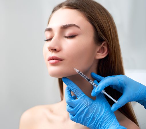 Smile lifting and lip augmentation. Beautician doctor hands doing beauty procedure to female face with syringe. Young woman's mouth countouring with filler injection. Marionette lines treatment in cosmetology clinic.